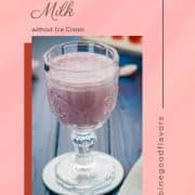 Cute and delicious pink strawberry milk in a gorgeous serving glass. Placed on a glass coaster on blue wooden ground.