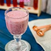 Cute and delicious pink strawberry milk in a gorgeous serving glass. Placed on a glass coaster on blue wooden ground.
