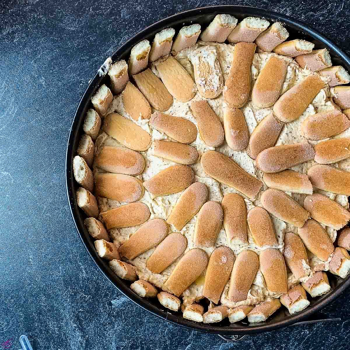 The layered almond cream cake with ladyfingers is ready to be chilled in the refrigerator.