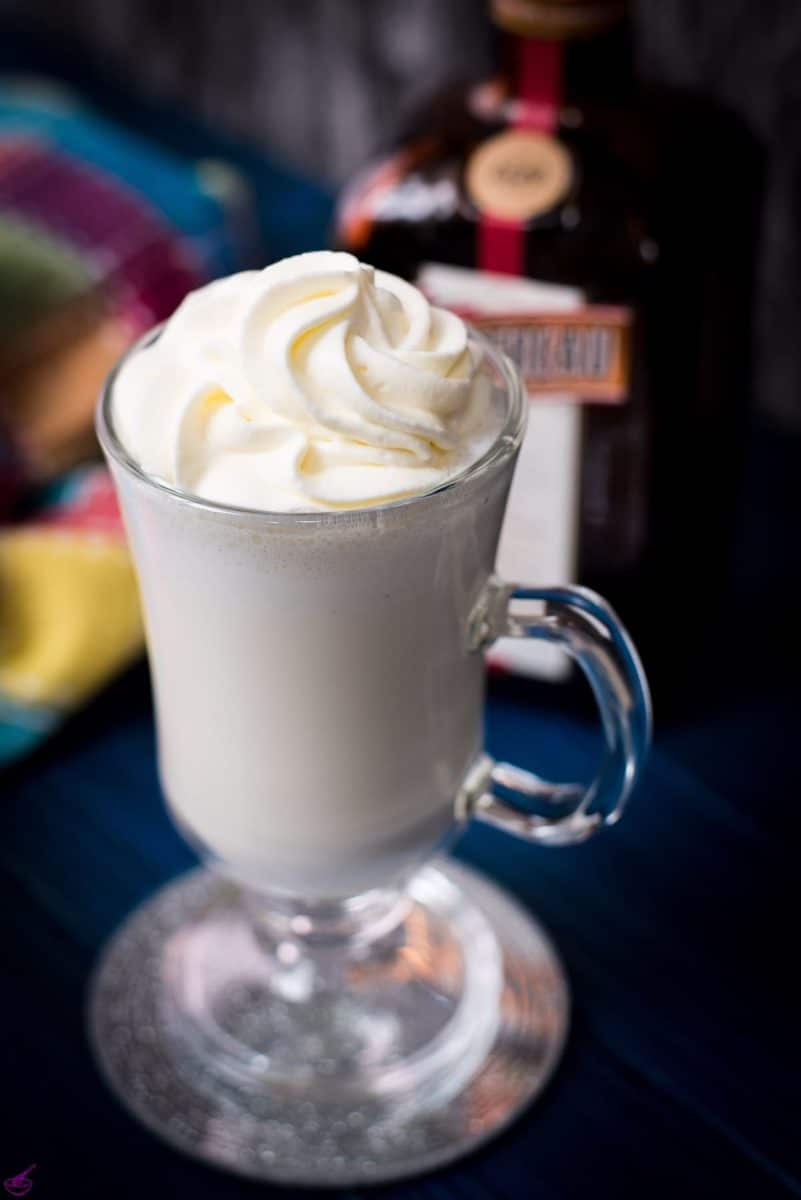 Delicious white Cointreau (orange liqueur) milkshake for adults on mirror glass coaster and dark blue wooden base.