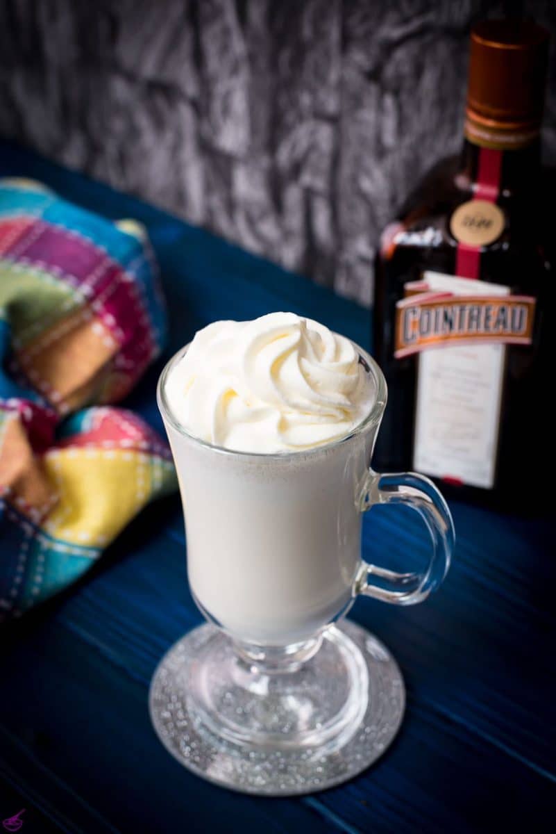 Delicious white Cointreau (orange liqueur) milkshake for adults on mirror glass coaster and dark blue wooden base.