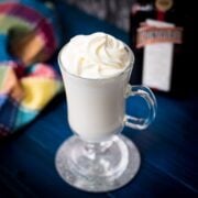 Delicious white Cointreau (orange liqueur) milkshake for adults on mirror glass coaster and dark blue wooden base.
