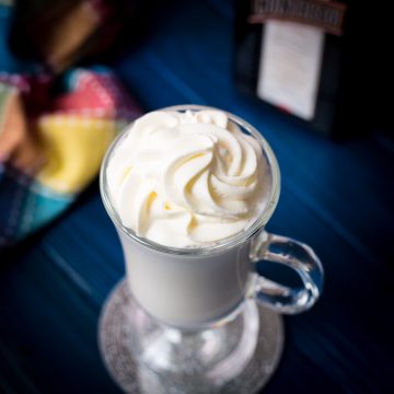 Delicious white Cointreau (orange liqueur) milkshake for adults on mirror glass coaster and dark blue wooden base.