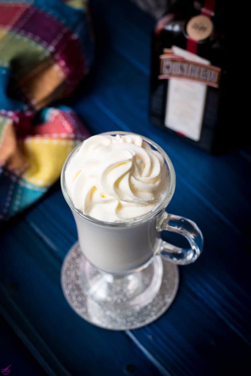 Delicious white Cointreau (orange liqueur) milkshake for adults on mirror glass coaster and dark blue wooden base.