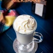 Delicious white Cointreau (orange liqueur) milkshake for adults on mirror glass coaster and dark blue wooden base.