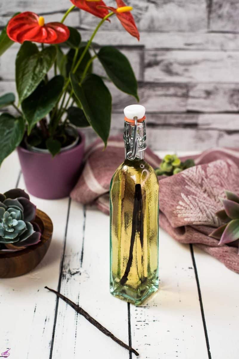 A beautiful bottle with amber-colored homemade vanilla vodka on a white wooden base.