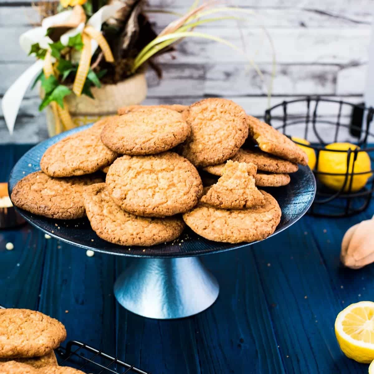 A pile of delicious lemon white chocolate chip cookies on blue cake stand. Standing on a blue wooden board, next to lemons and cookies.