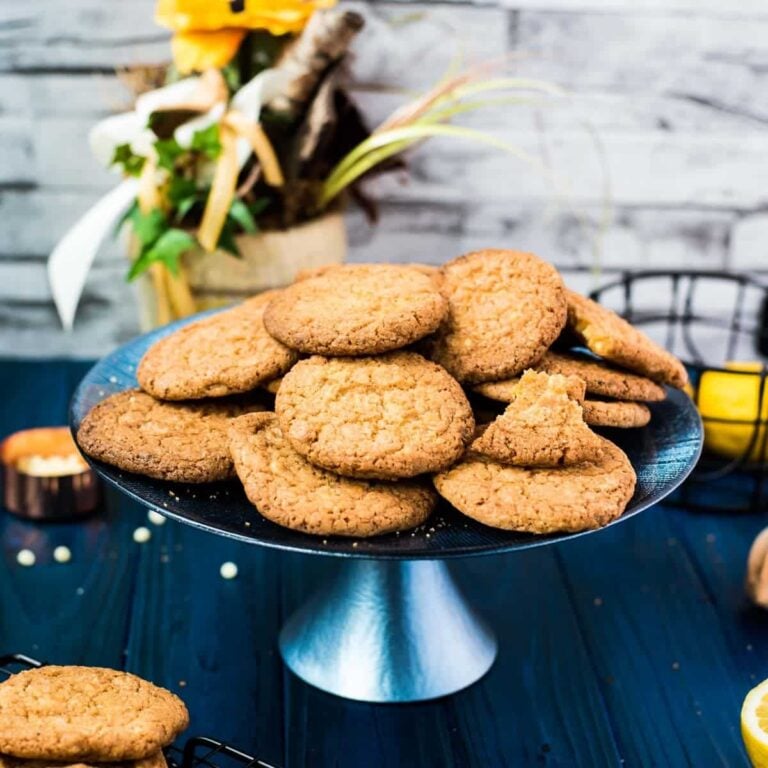 A pile of delicious lemon white chocolate chip cookies on blue cake stand. Standing on a blue wooden board, next to lemons and cookies.