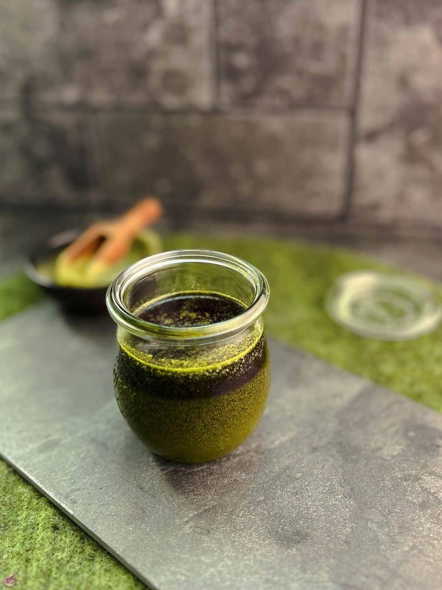 A preserving jar filled with Matcha butter (before cooling) on a slate plate.