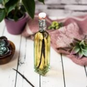 A beautiful bottle with amber-colored homemade vanilla vodka on a white wooden base.