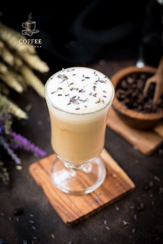 Gorgeous glass with honey lavender latte, sprinkled with dried lavender placed on wooden coaster.