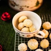 Melt-in-your-mouth butterball cookies on placed on cooling rack next to tea cup filled with butterball cookies.