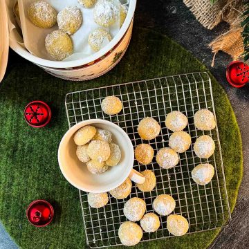 Melt-in-your-mouth butterball cookies on placed on cooling rack next to tea cup filled with butterball cookies.