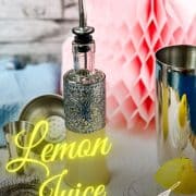 Bottle filled with freshly squeezed lemon juice fitted with a pouring spout, surrounded by cocktail making tools.