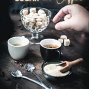 Two fingers dropping brown sugar cube into coffee mug.