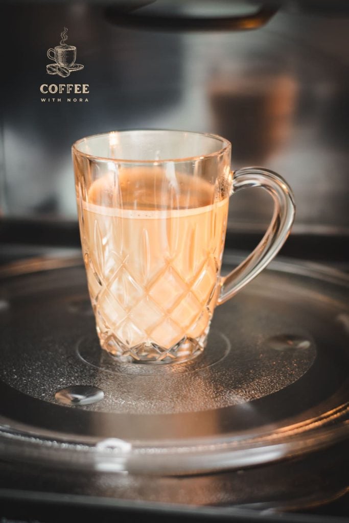 Glass mug filled with coffee and milk placed in microwave.