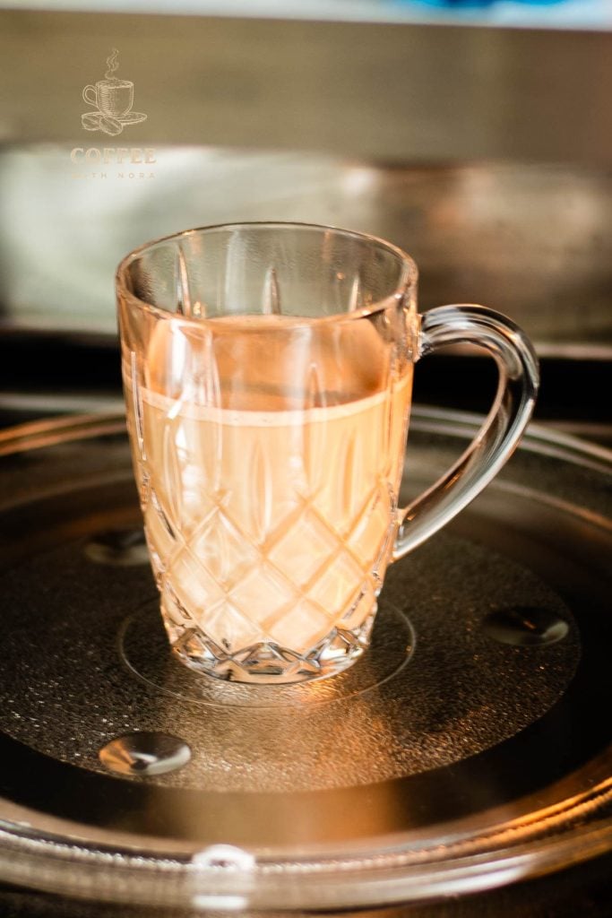 Glass mug filled with coffee and milk placed in microwave.