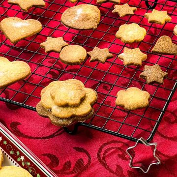 Delicious crispy sugar cookies on cooling rack, placed on Christmassy red tablecloth.