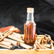 Preserving bottle filled with cinnamon dolce syrup, placed in wooden crate filled with cinnamon sticks.
