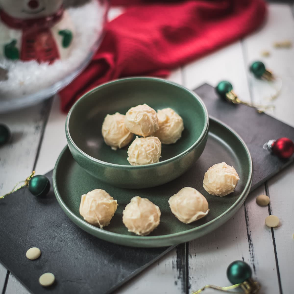Charming coconut truffles in green bowl next to Christmas decoration.