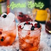 Two glasses filled with delicious cranberry Aaperol spritz, placed on snowy ground, garnished with a delicious berry mix.