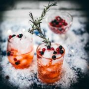 Two glasses filled with delicious cranberry Aaperol spritz, placed on snowy ground, garnished with a delicious berry mix.