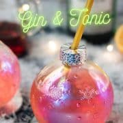 Gorgeous Christmas ornament shaped glass filled with festive cranberry gin tonic, placed on glass coaster.