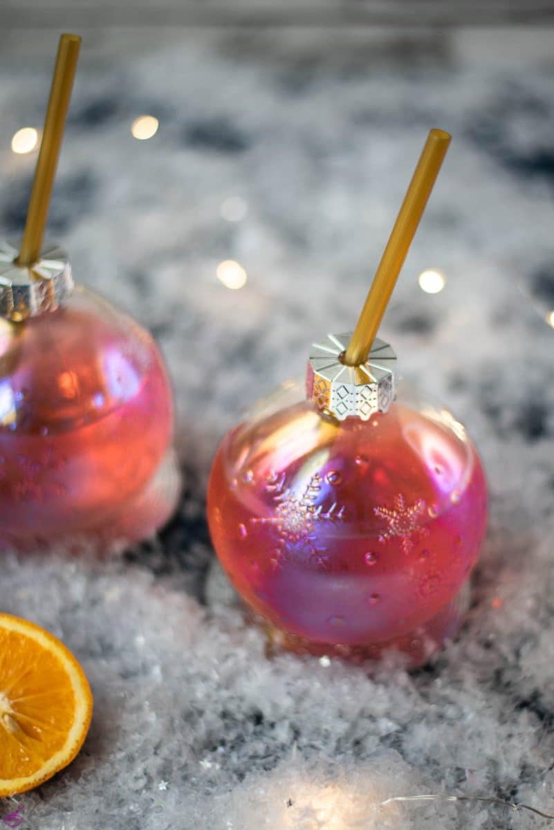 Gorgeous Christmas ornament shaped glass filled with festive cranberry gin tonic, placed on glass coaster.