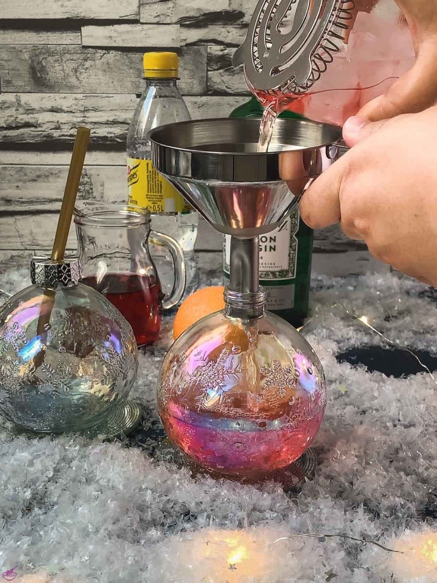 Fill up the Christmas ornament shaped glasses with cranberry gin tonic using a funnel.