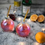 Gorgeous Christmas ornament shaped glass filled with festive cranberry gin tonic, placed on glass coaster.