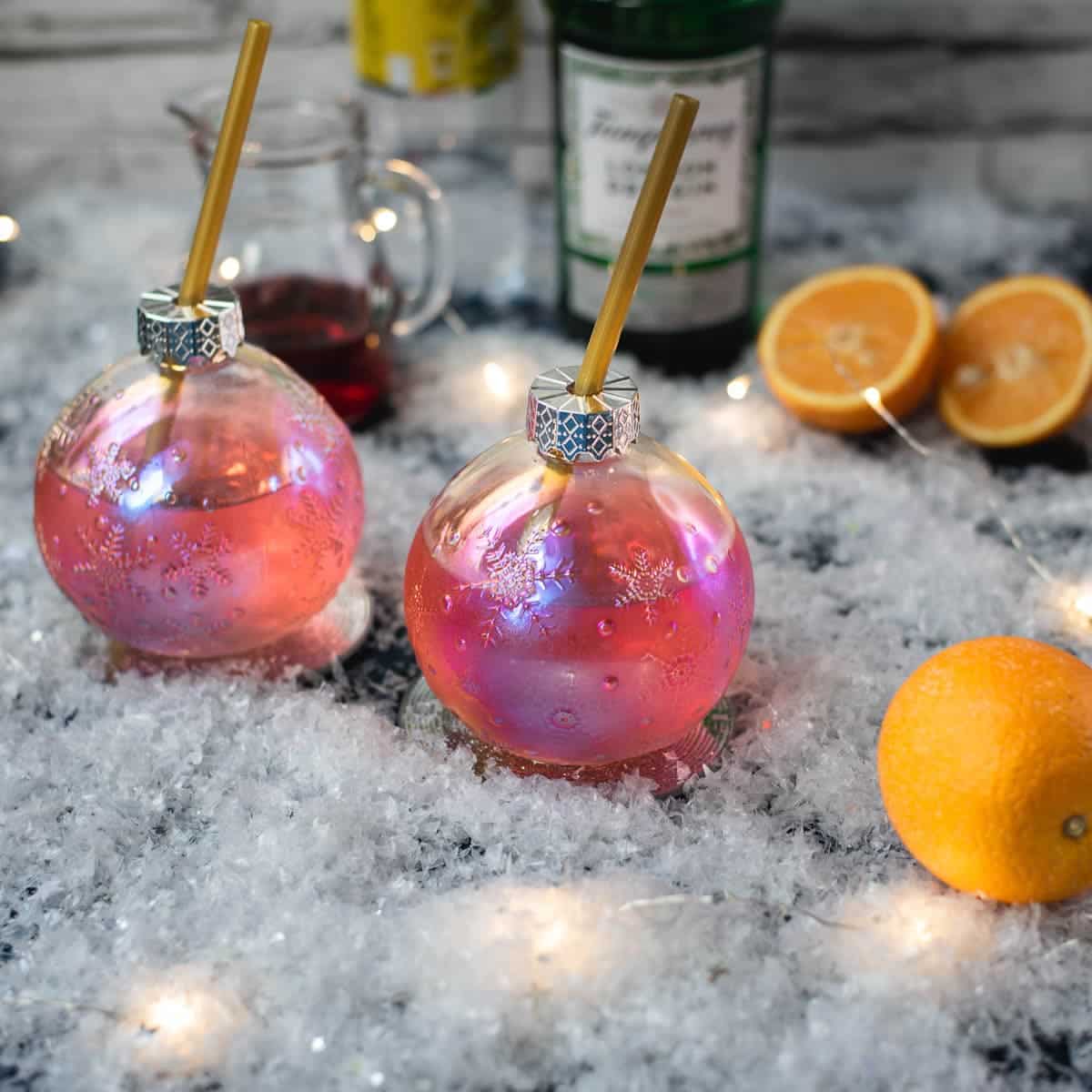 Gorgeous Christmas ornament shaped glass filled with festive cranberry gin tonic, placed on glass coaster.