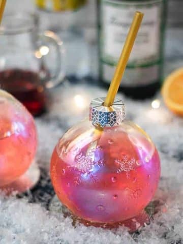 Gorgeous Christmas ornament shaped glass filled with festive cranberry gin tonic, placed on glass coaster.