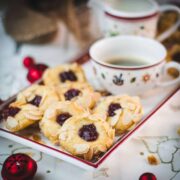 Delectable raspberry almond thumbprint cookies placed on Christmassy plate, next to a gorgeous cup of coffee.