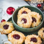 Delectable raspberry almond thumbprint cookies placed in a green bowl, next to red Christmas baubles.