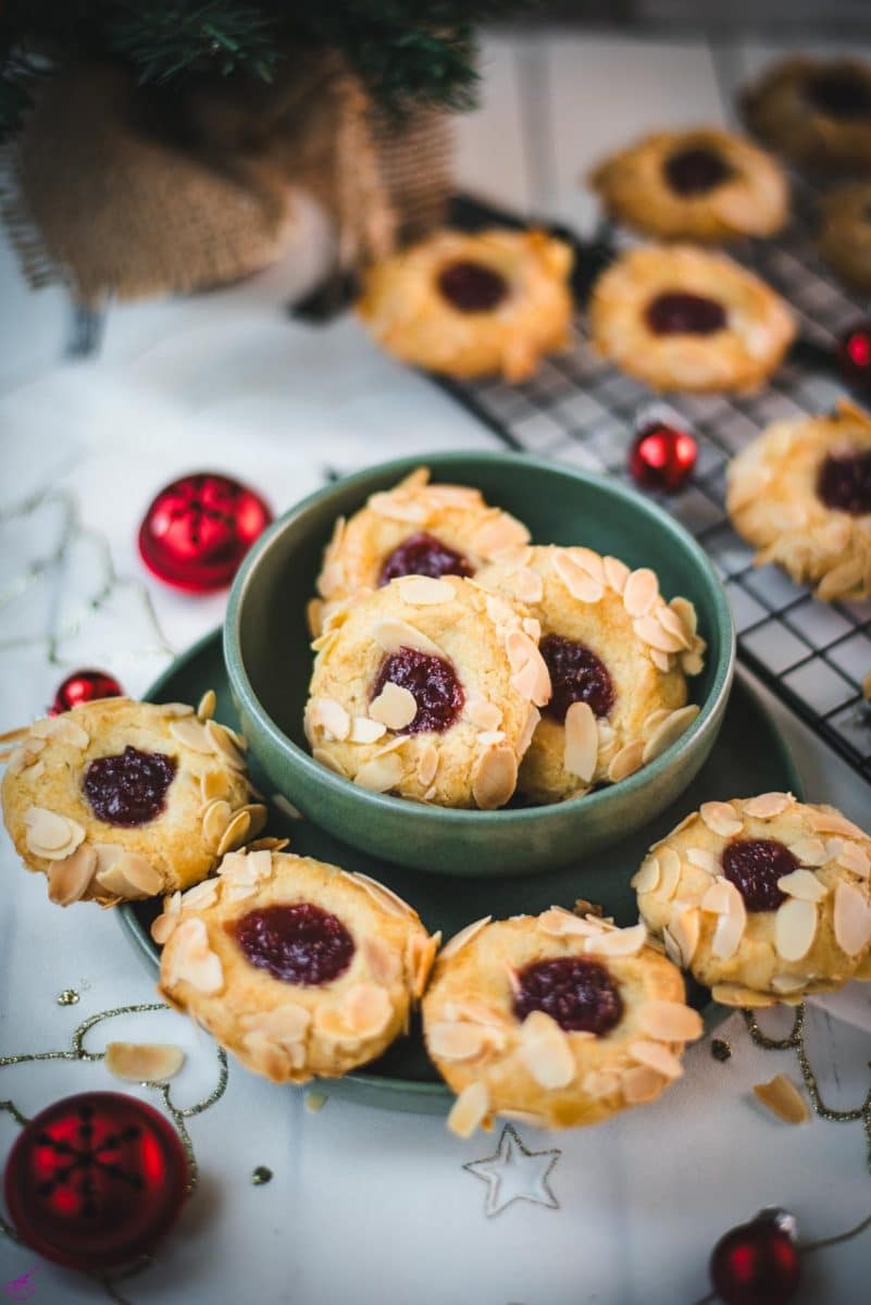 Delectable raspberry almond thumbprint cookies placed in a green bowl, next to red Christmas baubles.