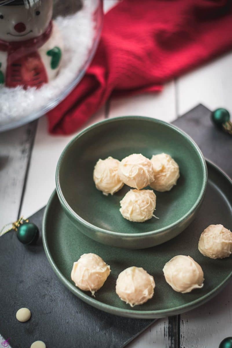 Charming coconut truffles in green bowl next to Christmas decoration.