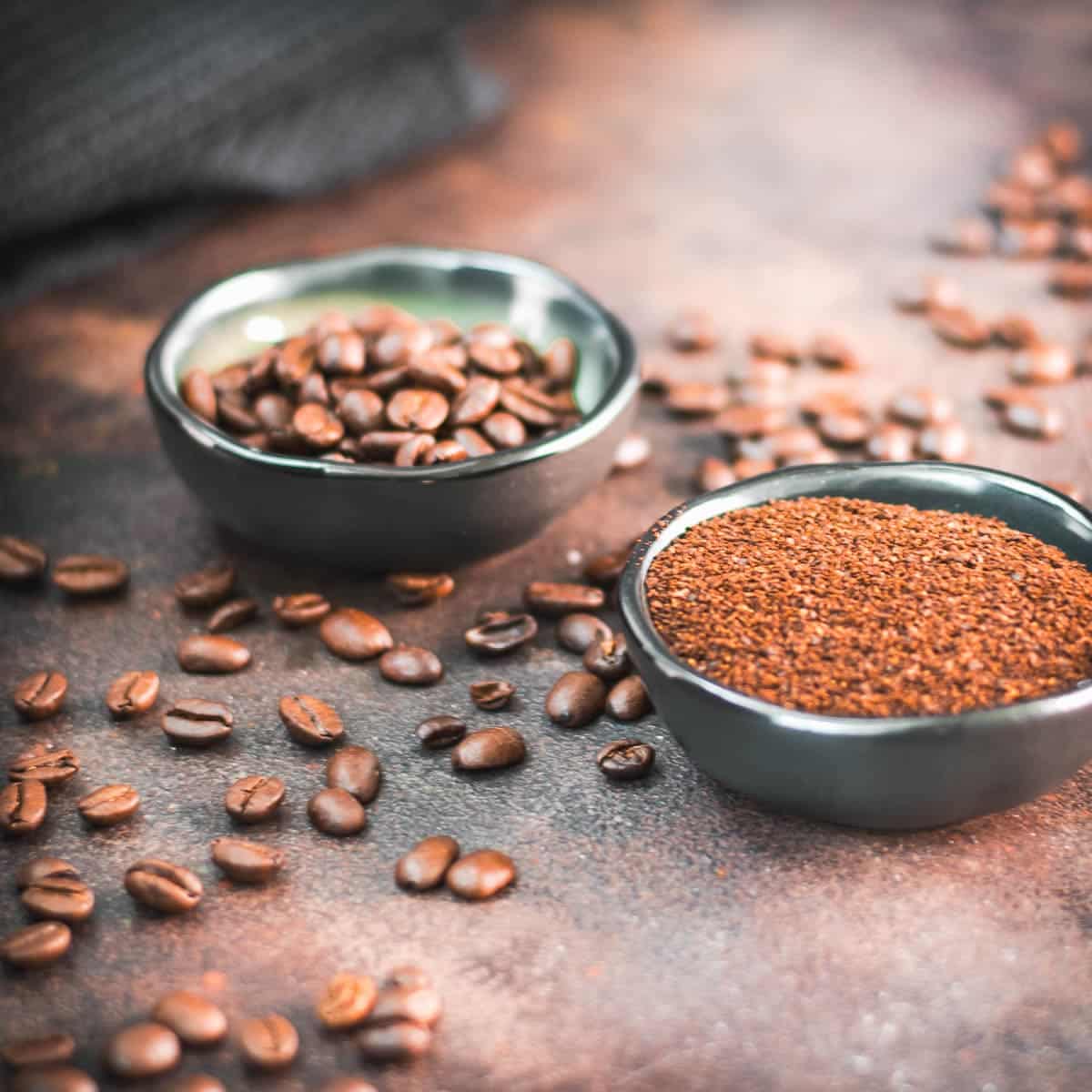 Two small bowls. One filled with ground coffee and one with coffee beans.