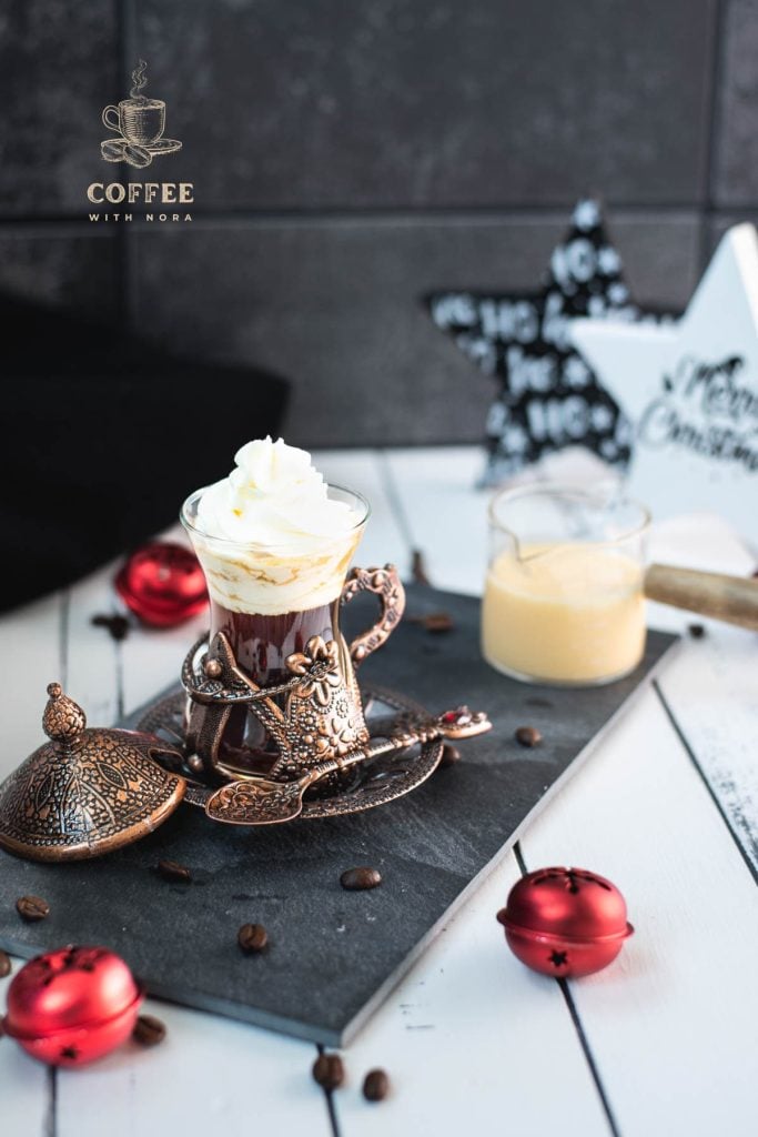 Gorgeous mediaeval coffee glass filled with black coffee, topped with eggnog flavored whipped cream. Placed on black slate plate next to a glass of eggnog.
