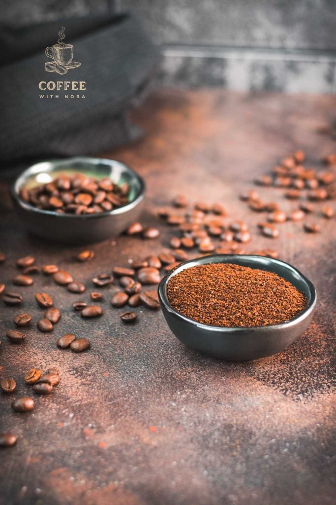 Two bowls each filled with coffee beans and grated coffee on rust brown background surrounded by coffee beans.