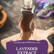 Curved bottle filled with homemade lavender extract on brown wooden board surrounded by lavender flowers.