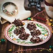 Christmas plate filled with dark chocolate clusters, on brown wooden background, next to Christmas decorations.