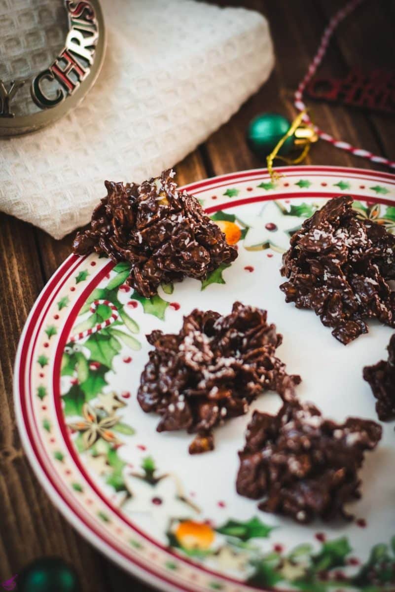 Christmas plate filled with dark chocolate clusters, on brown wooden background, next to Christmas decorations.