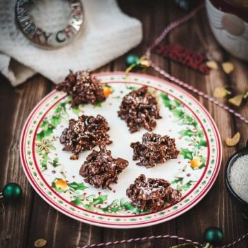 Christmas plate filled with dark chocolate clusters, on brown wooden background, next to Christmas decorations.