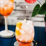 Wonderful layered Aperol Spritz! Tart and delicious! Placed on a mirror coaster on a blue wooden background.