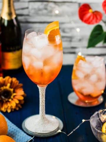 Wonderful layered Aperol Spritz! Tart and delicious! Placed on a mirror coaster on a blue wooden background.