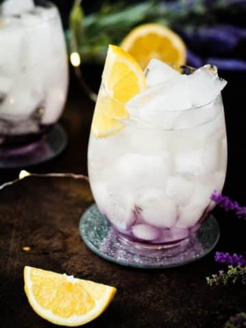 Gorgeous lavender spritz, garnished with lemon wedge and placed on shimmering coaster.