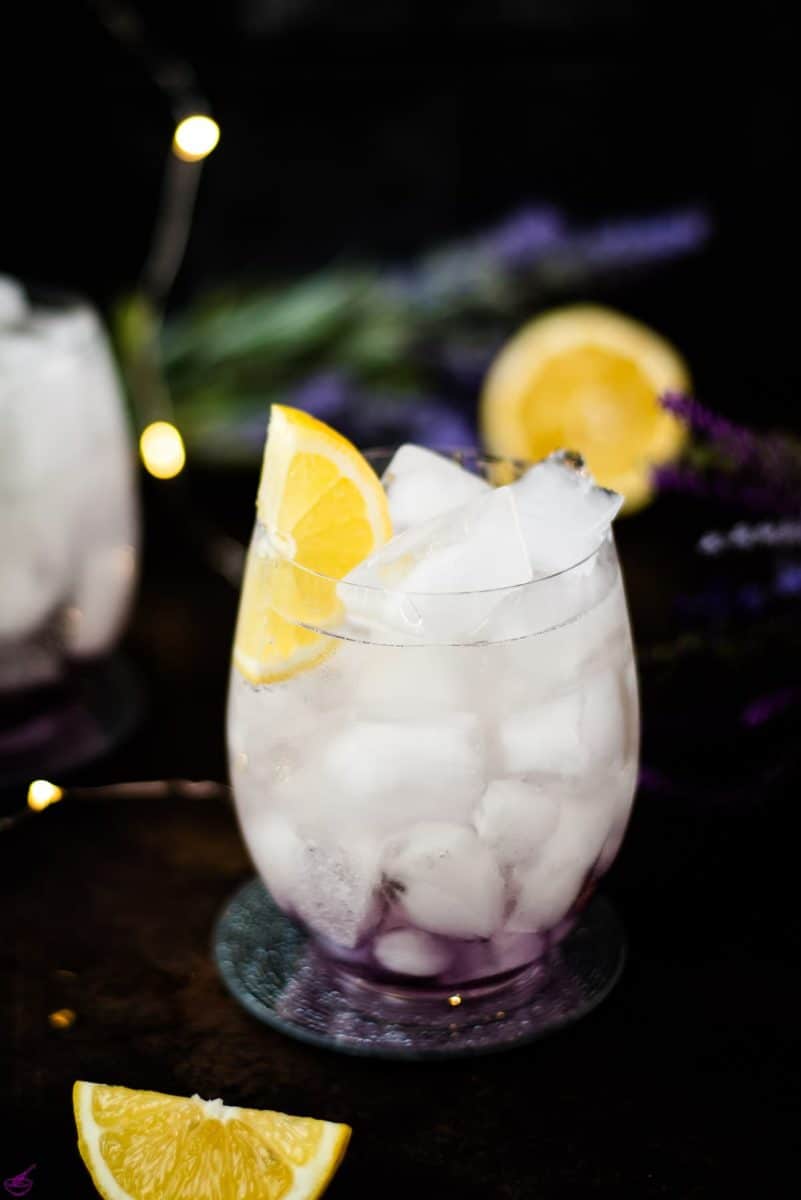 Gorgeous lavender spritz, garnished with lemon wedge and placed on shimmering coaster.