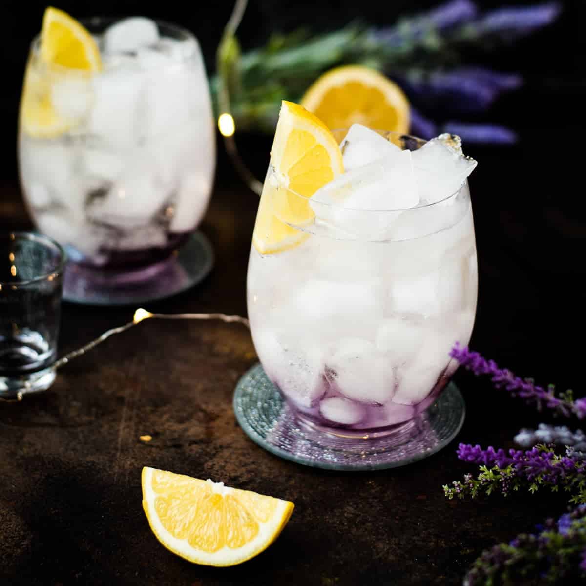 Gorgeous lavender spritz, garnished with lemon wedge and placed on shimmering coaster.
