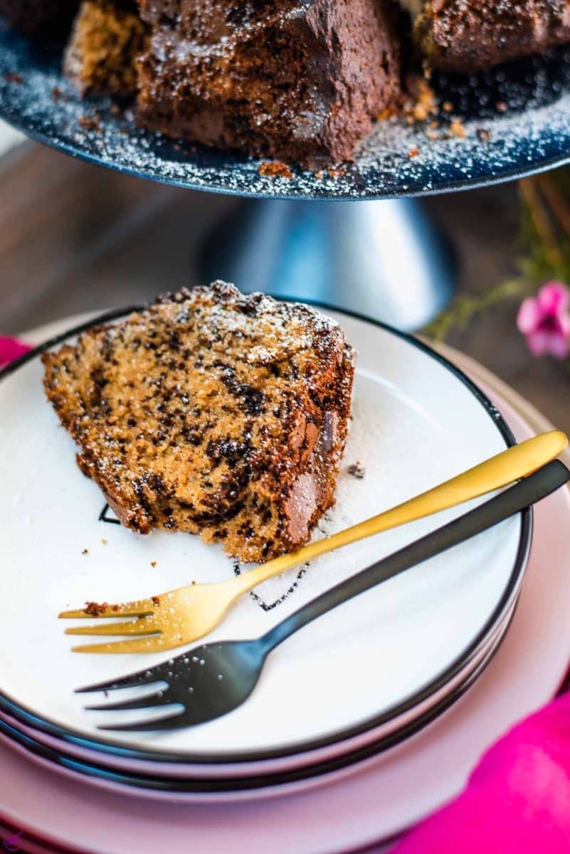 Gorgeous chocolate sprinkle spelt cake slice, placed on white plate, next to two forks, and dusted with powdered sugar.