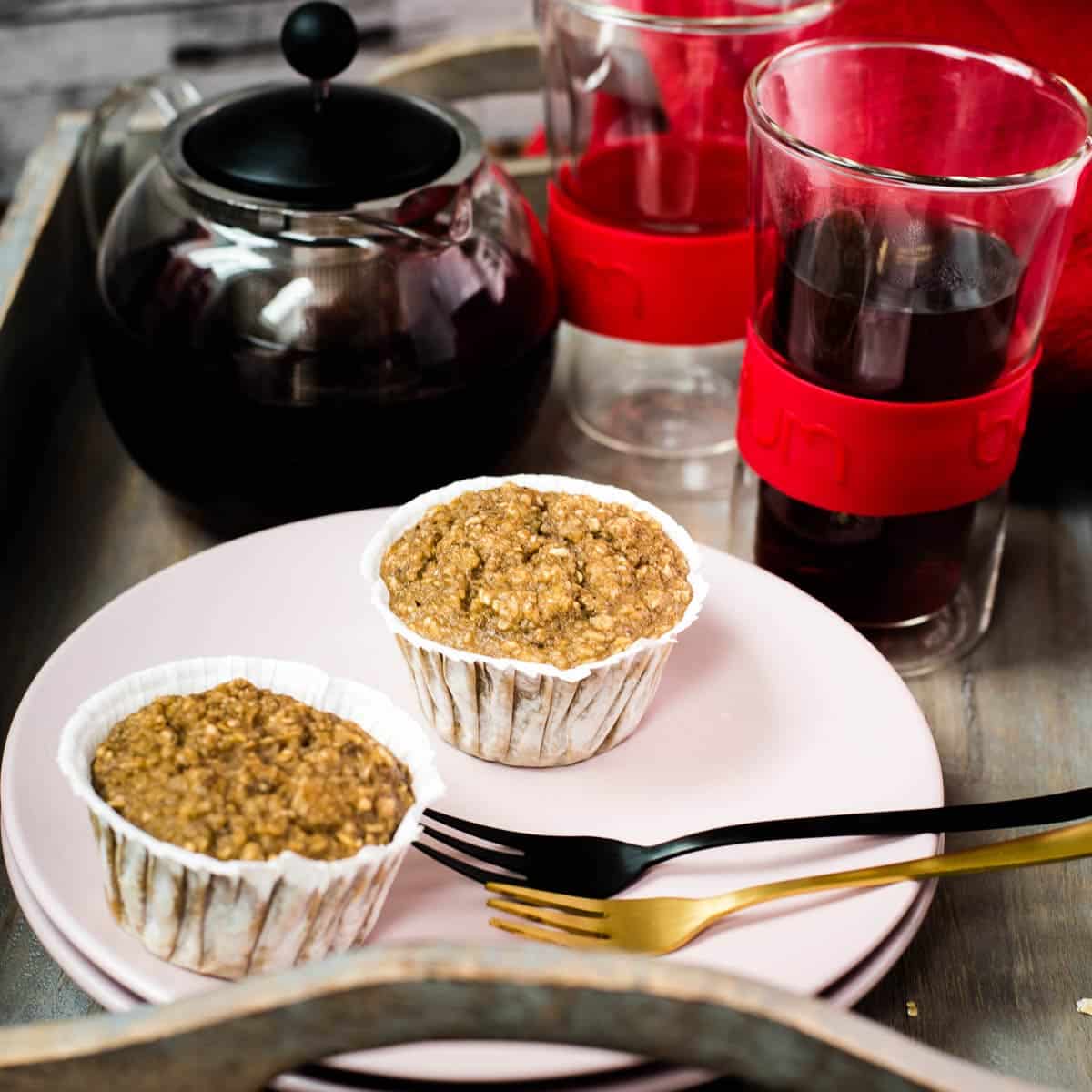 Two delicious banana oatmeal muffins on pink plate placed on wooden tray. Behind it, red fruit tee.